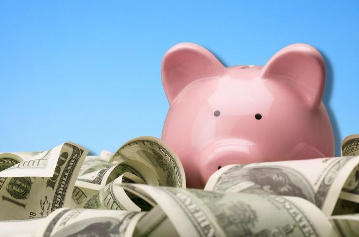 A piggy bank sits amongst various American dollar bills